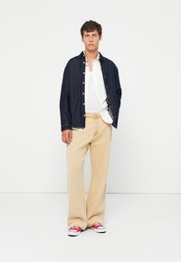Denim skjorte med knapper i marineblå, hvit tank topp, beige vide bukser og røde sneakers. Strukturert klær med avslappet passform og nøytrale toner.