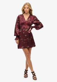 Vestido floral burdeos con mangas abullonadas, escote en V y detalles de botones. Fabricado en tejido ligero con patrones florales bordados. Sandalias negras con tiras.