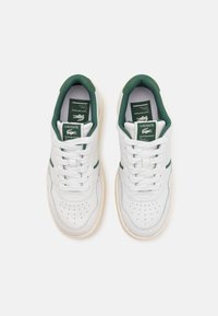 White leather sneakers with green accents, featuring a perforated toe, textured collar, and branded tongue label. Rubber sole.