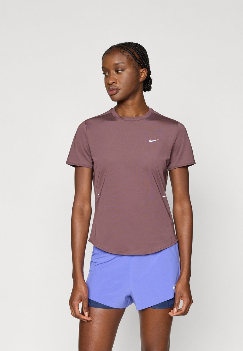 Καφέ κοντομάνικο πουκάμισο Nike με στρογγυλή λαιμόκοψη και διακοσμητικές ραφές στους ώμους. Συνδυάζεται με ανοιχτό μπλε σορτς και έχει μινιμαλιστικό σχεδιασμό.