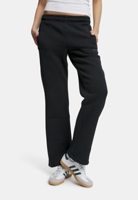 Sorte joggebukser med en avslappet passform, elastisk midje og sidelommer; med en subtil logo foran og en jevn tekstur.