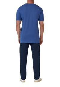 Blauwe T-shirt met korte mouwen, ronde hals en een comfortabele pasvorm, gecombineerd met donkere marineblauwe broek en witte schoenen, wat een casual outfit laat zien.