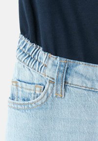 Jasnoniebieskie dżinsowe spodnie z elastycznym pasem i małą przednią kieszonką, zestawione z ciemnogranatową bluzką włożoną do środka.