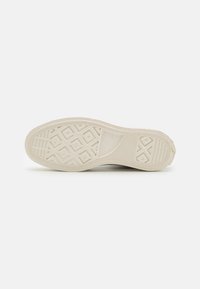 Rubber shoe sole in off-white with a textured surface, featuring a geometric pattern and clear tread design for traction.