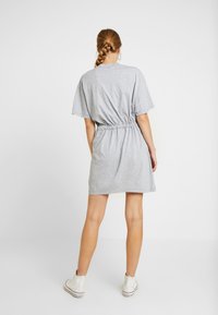 Grå klänning med korta ärmar och elastiskt midjeband. Gjord av mjukt material, med en avslappnad passform som når till mitten av låret, i kombination med vita sneakers.