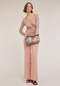 Haut à manches longues en maille rose clair, à enrouler, associé à un pantalon large pêche fluide. Comprend un sac à main en imprimé serpent noir et beige avec une bandoulière en chaîne.