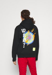 Sudadera negra con capucha que presenta un gráfico colorido de baloncesto con llamas y el texto "¿WNO?" en la parte de atrás. Parte frontal lisa y puños acanalados.