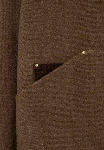 Tissu en mélange de laine marron avec une poche rectangulaire doublée de velours côtelé, rehaussée par deux clous en métal.