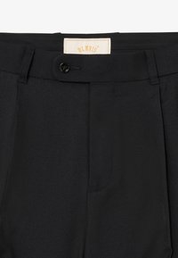 Pantalones negros ajustados con cierre de botón, dos pliegues frontales y una etiqueta cosida en el interior de la cinturilla. Textura suave y color sólido.