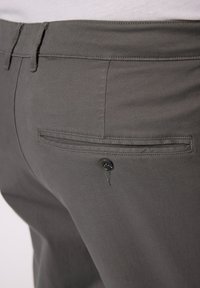 Graue Hose mit glatter Textur, ausgestattet mit einer Gesäßtasche mit Knopfverschluss und subtilen Nähten entlang der Kante.