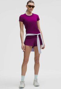 Lilla sport T-särk ja sobivad lühikesed püksid, valge sidumisvööga; koos helesiniste sokkide ja hallide tossudega; sile tekstuur.