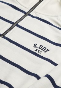 Witte trui met marineblauwe horizontale strepen, voorzien van een ritskraag en borduursel van het "S.DRY N.Y.C." logo op de borst. Zachte textuur.