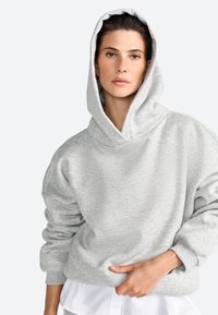 Sivá oversized mikina vyrobená z mäkkej látky, s veľkou kapucňou, rebrovanými manžetami a jemnými ozdobami na prednej časti textúry.