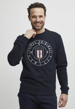 Felpa blu navy con colletto rotondo, maniche a costine, con un logo grafico centrale che presenta uno scudo, numeri e lettere direzionali.