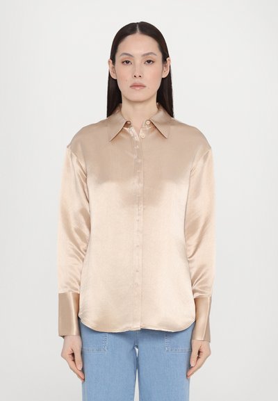 Chemise boutonnée en satin beige avec un col classique, des manches longues et un ourlet arrondi, affichant une texture lisse et un léger éclat.