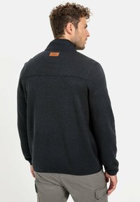 Donkergrijs fleecejack met een opstaande kraag, voorzien van een leren patch op de rug en subtiele stikseldetails. Casual en comfortabel ontwerp.
