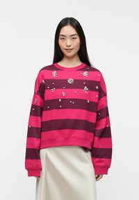 Sweatshirt listrado em rosa e bordô, com detalhes e texturas, gola redonda canelada e costuras de ombros caídos.