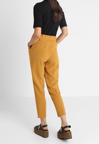 Rostfärgade skräddarsydda byxor med slim fit och sidofickor, i kombination med en svart ribbad topp och svarta plattformsandaler.