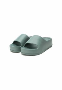 Chanclas verdes de plástico moldeado con la punta abierta y correas anchas. Suela gruesa de plataforma con fondo texturizado para agarre. Acabado mate suave.