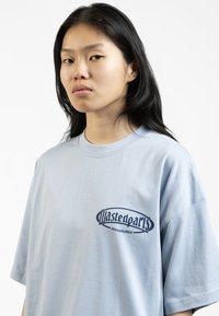Light blue cotton t-shirt featuring a dark blue logo on the left chest. The design has a relaxed fit and short sleeves.