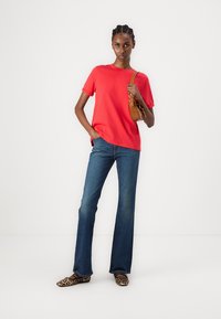 Rød bomull t-skjorte, løs passform, sammen med mørkeblå utsvingte jeans. Brukt med leopardo-mønstrede flate sko og en liten brun håndveske.