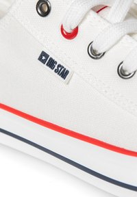 Weißes Canvas-Sneaker mit roten Akzenten, schwarzen Ösen und einem blauen Streifen entlang der Sohle. Verfügt über ein "BIG STAR"-Logoschild.