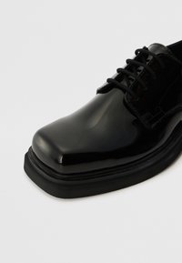 Zwarte gepatineerde leren schoen met een ronde neus, vetersluiting en een gestructureerde zwarte rubberen zool. Glad oppervlak met een glanzende afwerking.
