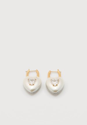 Zlaté kruhové náušnice s príveskami v tvare perlových sŕdc, každé s čírym krištáľom v tvare srdca v strede, na jednoduchom bielom pozadí.