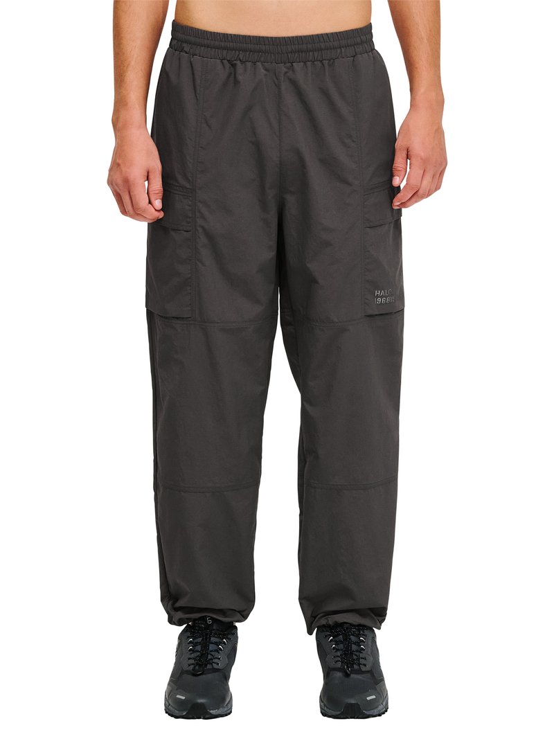 Mand iført sorte cargobukser med elastisk talje og sorte vandresko, stående foran en hvid baggrund.