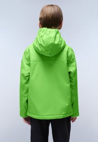 Bambino che indossa una giacca con cappuccio verde brillante e pantaloni neri, in piedi con le spalle alla macchina fotografica, contro uno sfondo semplice.