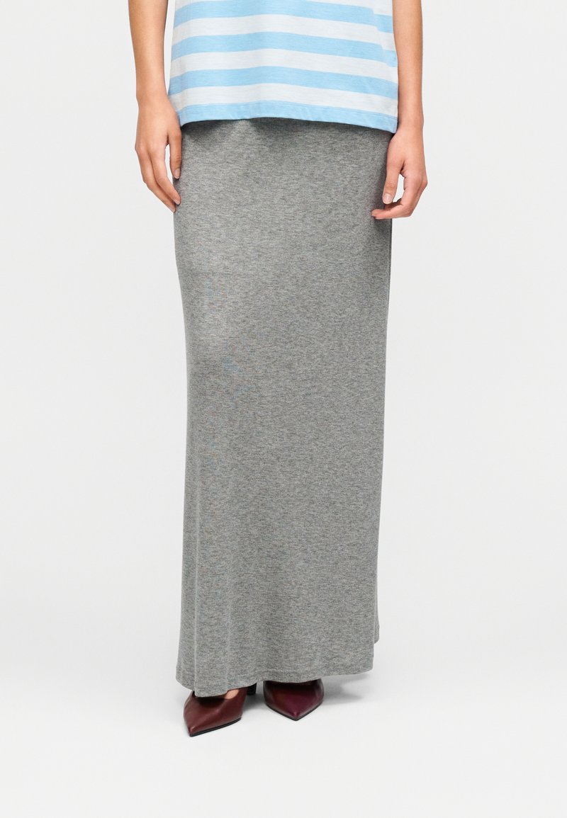 Jupe en maille grise mi-genou avec une texture douce, associée à des talons pointus bordeaux. La tenue est complétée par un haut bleu à rayures horizontales.