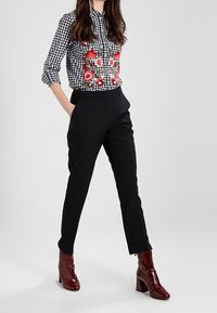 Svart och vit rutig skjorta med röd blommig broderi, kombinerad med slim fit svarta byxor och vinröda ankelstövlar, mot en neutral bakgrund.