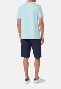 Jasnoniebieska koszulka z krótkim rękawem, w zestawie z granatowymi szortami i białymi trampkami. Miękki materiał, luźny krój, prosty design bez wzorów.