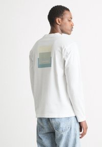 Tricou alb din bumbac cu mâneci lungi, având un grafic colorat pe spate cu textul "Calvin Klein" și o croială relaxată.