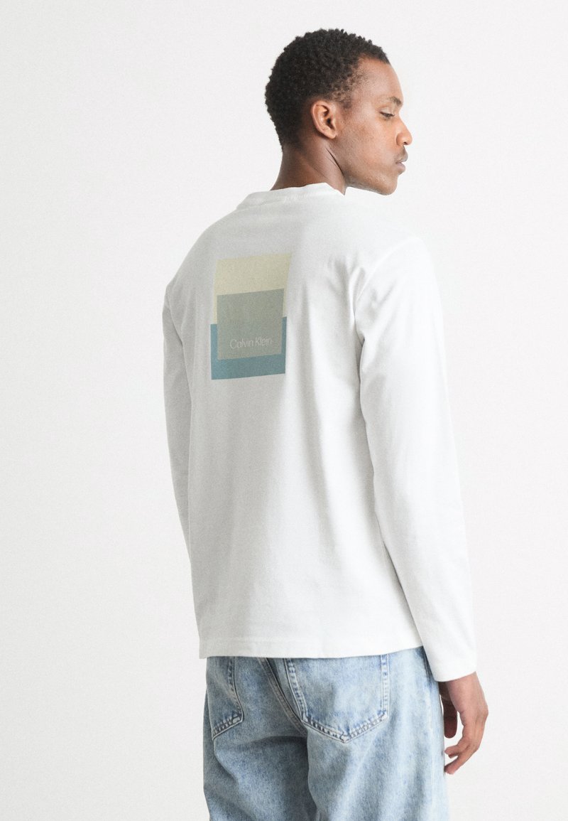 Tricou alb din bumbac cu mâneci lungi, având un grafic colorat pe spate cu textul "Calvin Klein" și o croială relaxată.