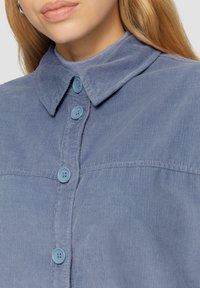 Blauw corduroy overhemd met een klassieke kraag, voorzien van drie knoopsluitingen in een bijpassend blauw. Gestructureerde stof met fijne verticale ribbels.