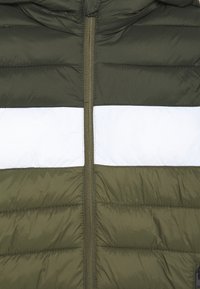 Zbliżenie na oliwkową kurtkę puchową z poziomym białym paskiem na klatce piersiowej i centralnym zamkiem błyskawicznym.