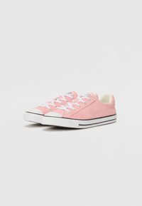 Rosa Wildledersneaker mit weißen Schnürsenkeln, einer weißen Zehenkappe und einer Sohle mit schwarzen Streifen. Niedriges Design mit glatter Textur und minimaler Markenkennzeichnung.