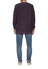 Lila langärmliger Pullover mit gerippten Bündchen und Saum, kombiniert mit hellblauen Jeans und weißen Sneakern. Der Pullover hat ein strukturiertes Strickdesign.