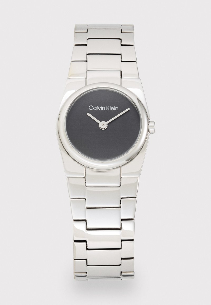 Silver metallarmbandsur med en rund, svart urtavla. Funktioner inkluderar två silverhänder och texten "Calvin Klein" på urtavlan.