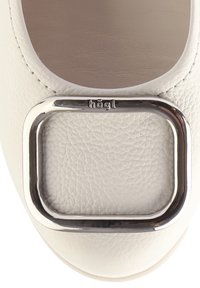 Vita läderballetskor med en stor rektangulär metallspänne vid tån och texturerad ovansida. Varumärke synligt på sidan.