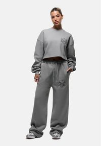 Grijze cropped sweatshirt en bijpassende sweatpants, met een losse pasvorm, zachte textuur en een decoratieve zwarte grafiek op de borst en bovenbeen.