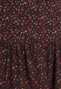 Tissu foncé avec un petit motif floral rouge, marron, blanc et rose, et une texture côtelée verticale subtile, froncé à la couture horizontale.