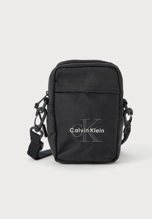 Mustast kangast rihmkott luku, reguleeritava rihma ja esiküljel reljeefse "Calvin Klein" logoga. Kompaktne ristkülikukujuline vorm.