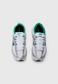 White Nike sneakers with mesh upper, silver accents, green inner lining, and white laces. Features curved design and textured sole.