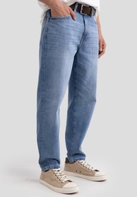 Jean en denim bleu clair avec une coupe droite, présentent des poches avant et une ceinture en cuir marron, associées à des baskets beiges.