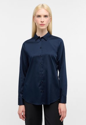 Marineblaue Seidenbluse mit Knopfleiste, langen Ärmeln, Kragen und abgerundetem Saum. Glatte Textur; subtile, schimmernde Oberfläche.