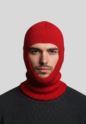 Red knitted balaclava with a seamless design, featuring a ribbed texture around the face and neck, worn over a dark grey sweater.