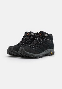 Czarne buty trekkingowe z wysokim krojem, z wytrzymałą podeszwą, teksturowanym wierzchem, wzmocnionymi oczkami oraz pomarańczowymi akcentami.