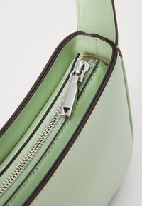 Sac à main en simili cuir vert avec une fermeture éclair noire contrastante, fermeture zippée et texture lisse. Il est doté d'une bandoulière robuste.